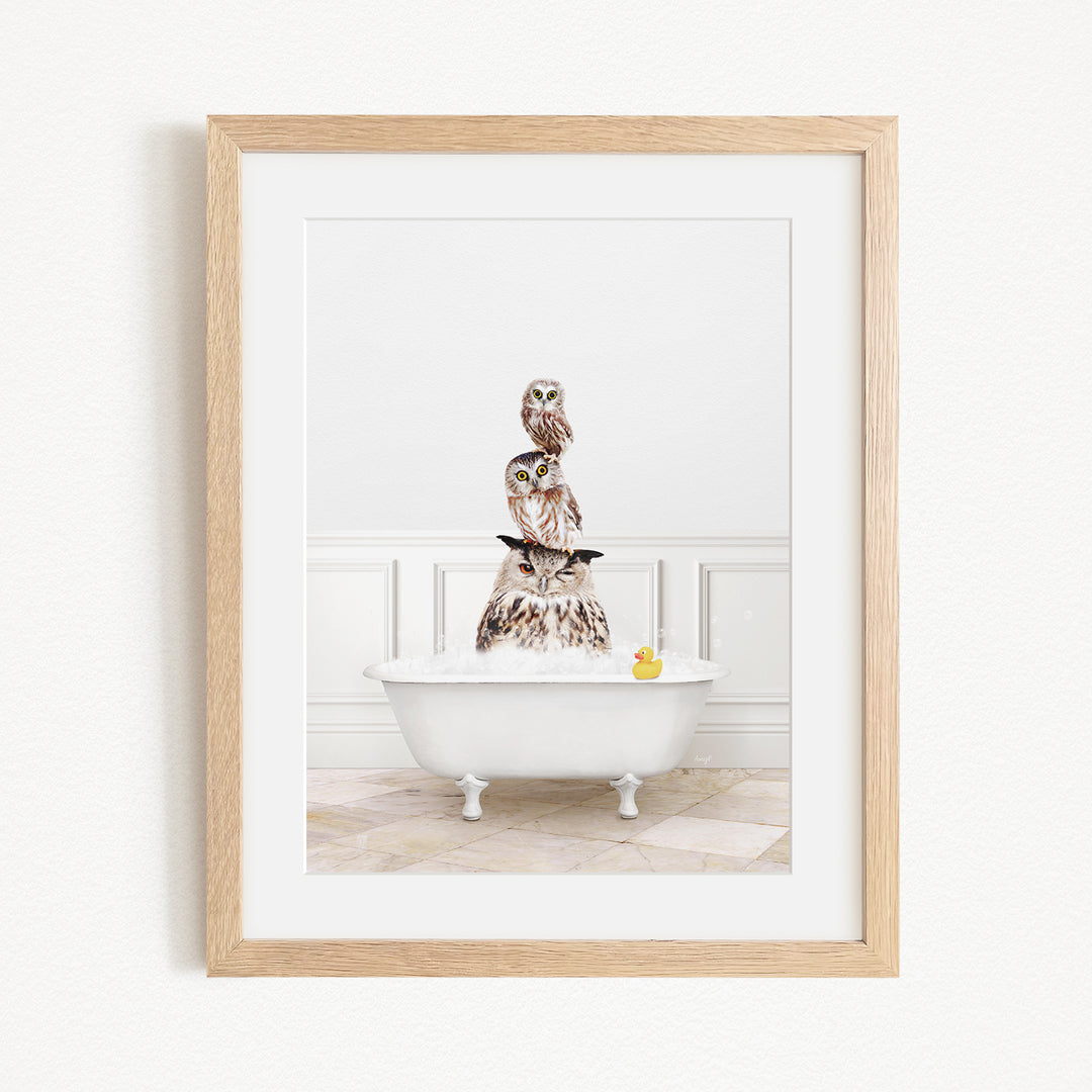 A framed image depicting a white bathtub filled with water, with a stack of owls sitting on top of it.