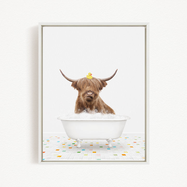 A brown cow with long horns is sitting in a white bathtub filled with bubbles, with a rubber duck perched on its head.
