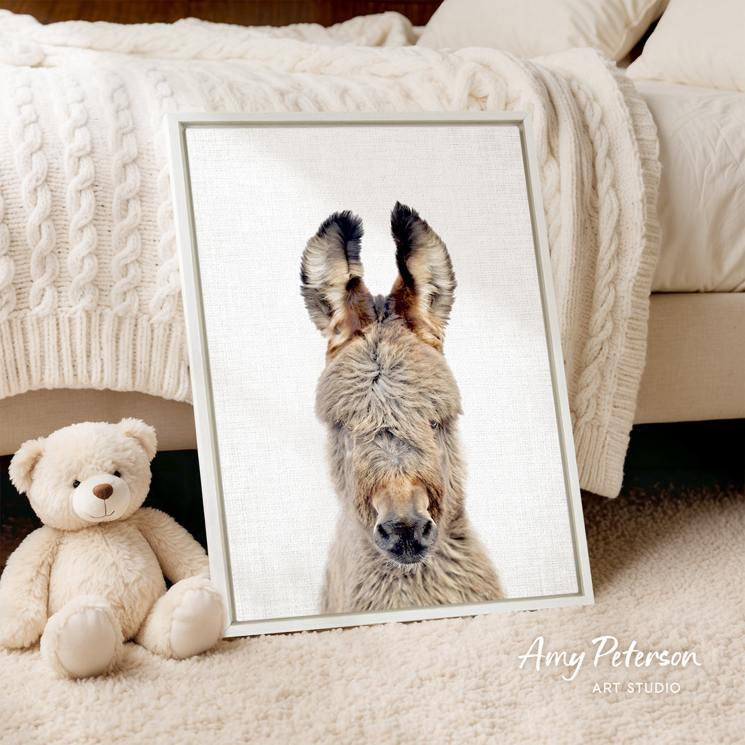 A framed photograph of a donkey is displayed on a white bedspread, accompanied by a teddy bear on the floor.