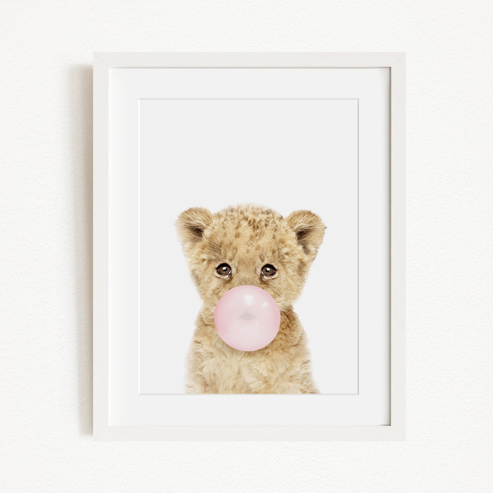 A cute baby lion blowing a bubble with a pink bubble gum bubble.
