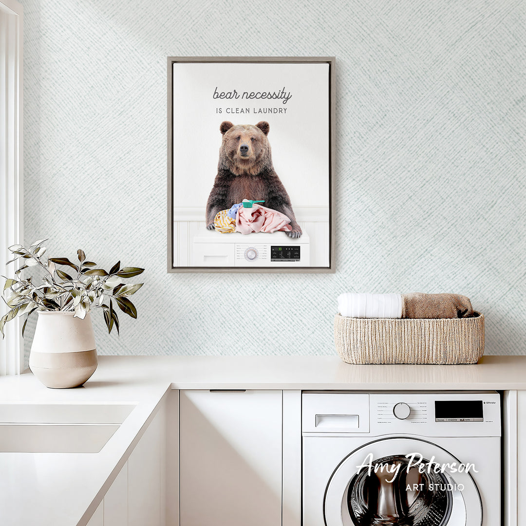 a framed poster of a bear sitting on a laundry basket, with the text "bear necessity is clean laundry" displayed above the bear.