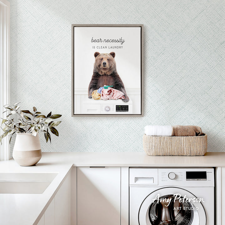 a framed poster of a bear sitting on a laundry basket, with the text "bear necessity is clean laundry" displayed above the bear.