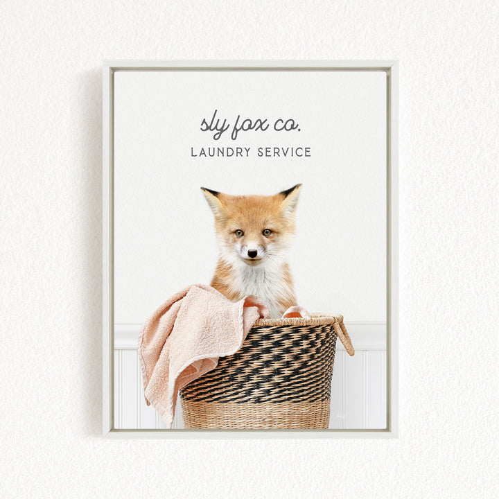 A young fox sits in a woven laundry basket, with a towel draped over its back.