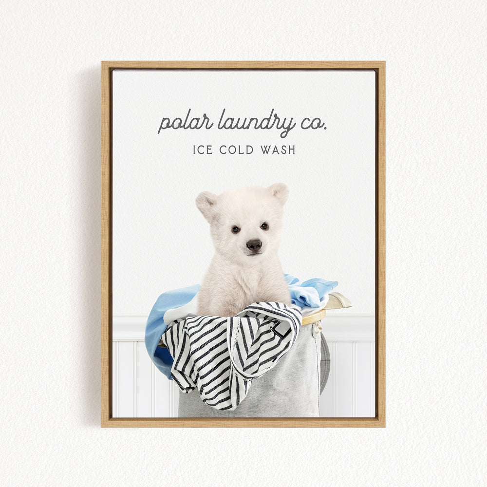 A polar bear sitting in a laundry basket, with a blue and white striped towel and a blue and white striped shirt inside the basket.