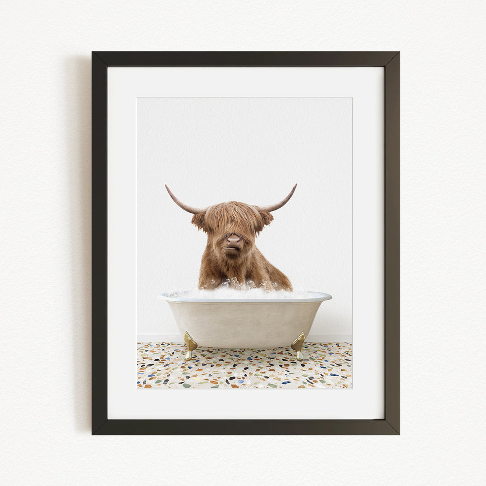 A Highland cow with long horns is sitting in a white bathtub filled with water, creating a whimsical and playful scene.