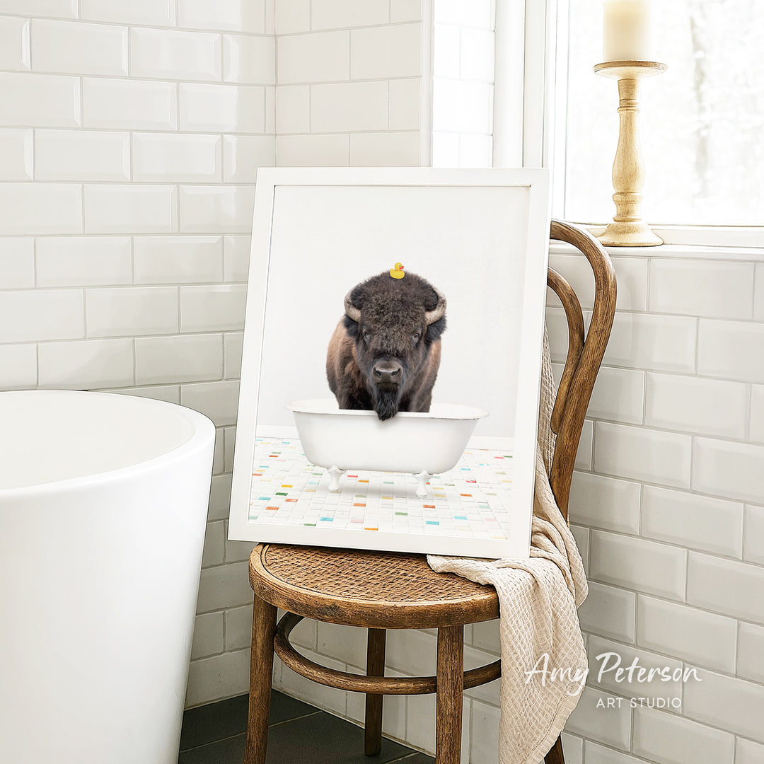 A framed image of a bison sitting in a white bathtub, with a yellow rubber duck floating on the water.