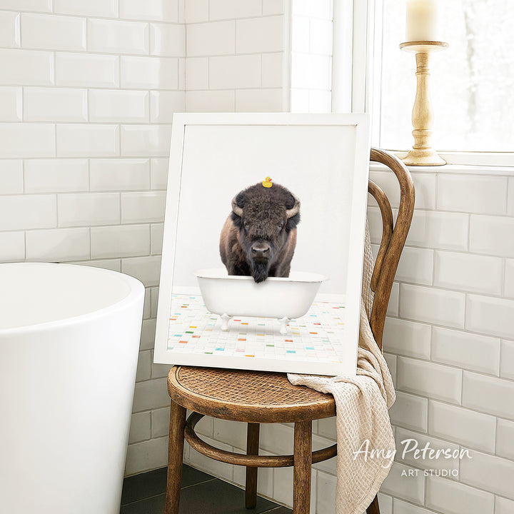 A framed image of a bison sitting in a white bathtub, with a yellow rubber duck floating on the water.