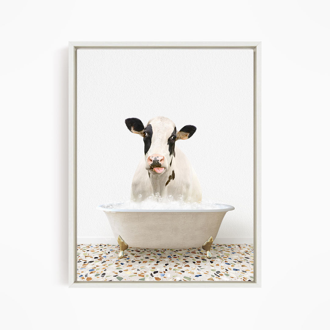 A black and white cow is sitting in a white bathtub filled with water, creating a whimsical and humorous scene.