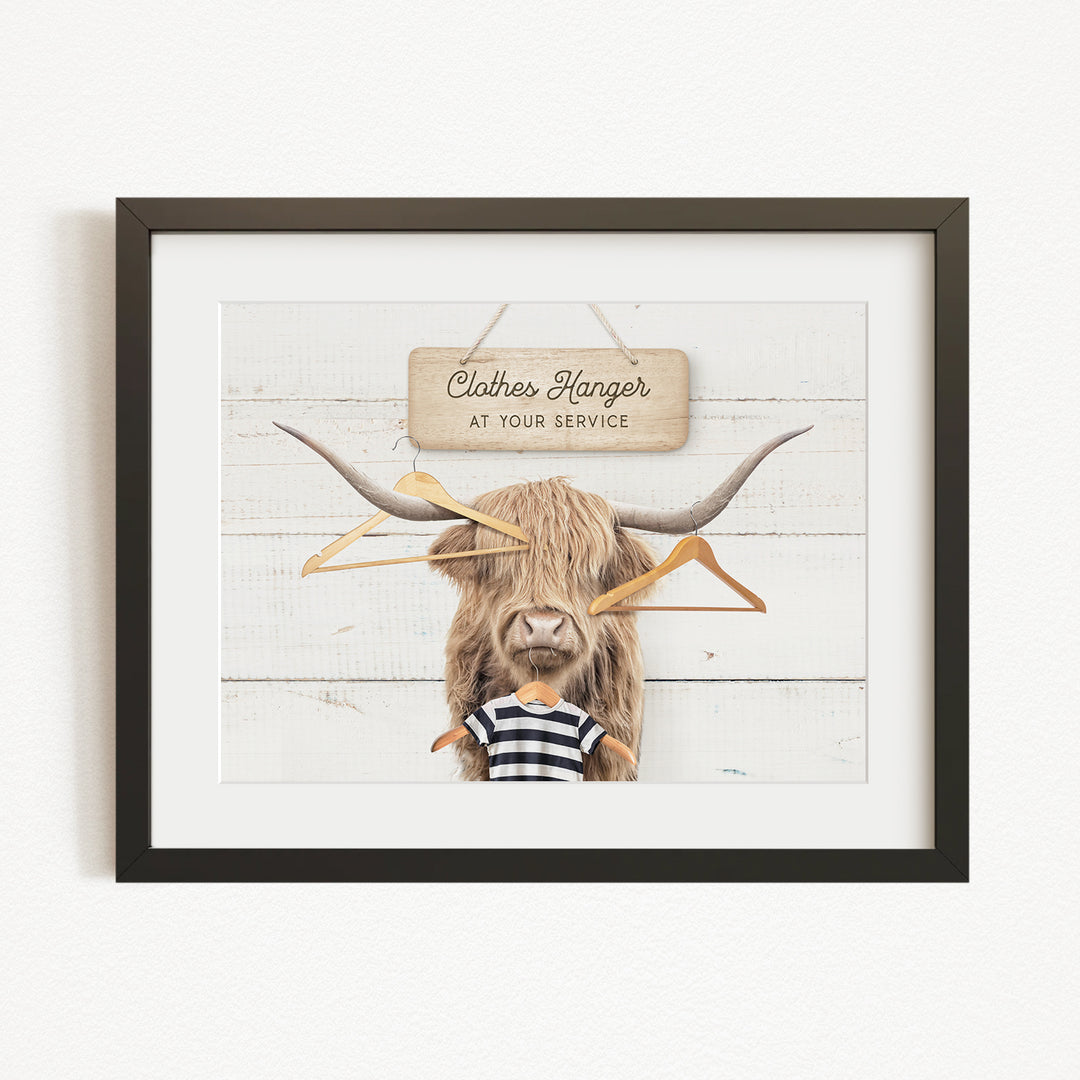 A framed image depicting a large, furry animal with a sign that reads "Clothes Hanger at your service" in front of it.