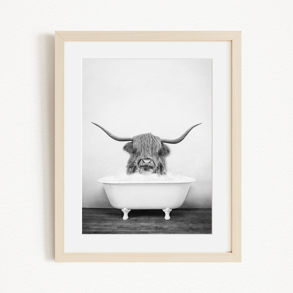 A black and white photograph of a horned animal, possibly a yak or a bison, sitting in a white bathtub and enjoying a bath.