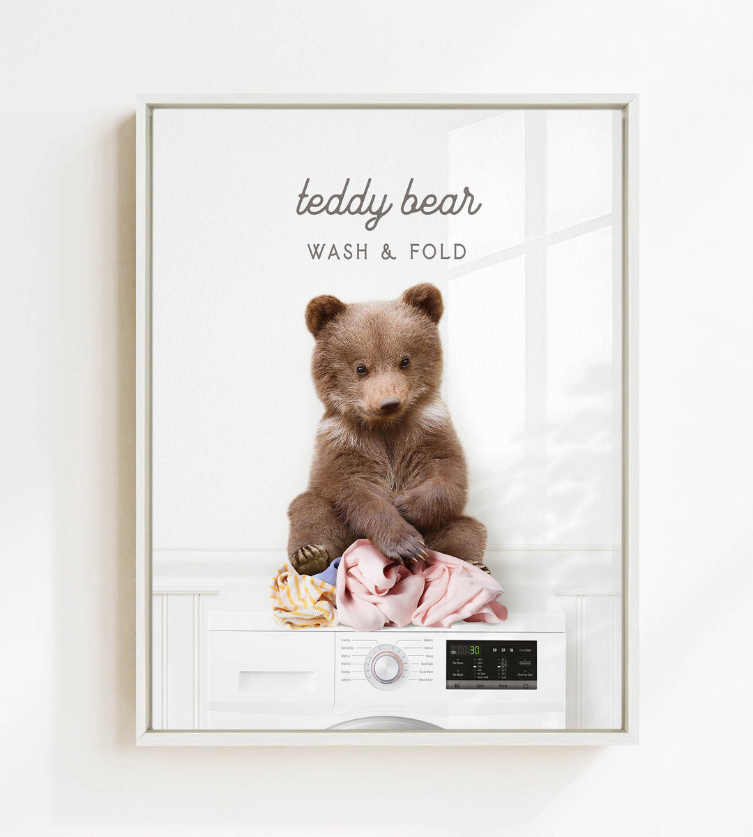 A teddy bear sitting on a pile of laundry next to a washing machine, with the text "teddy bear WASH & FOLD" displayed above the bear.