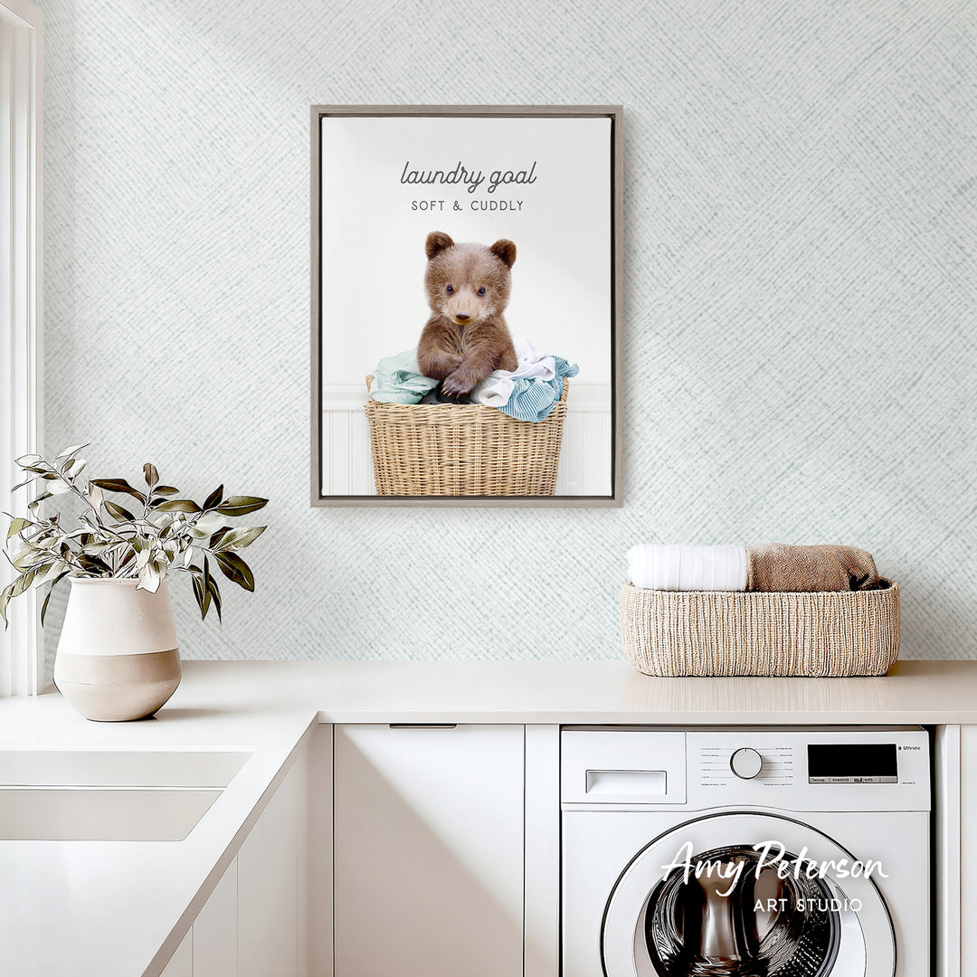a framed picture of a cute bear sitting in a wicker basket, placed on a white countertop in a laundry room.
