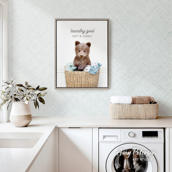 a framed picture of a cute bear sitting in a wicker basket, placed on a white countertop in a laundry room.