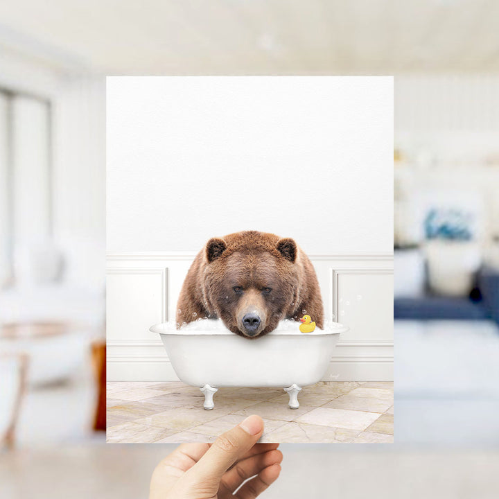 A brown bear is sitting in a white bathtub, with a yellow rubber duck floating in the water.
