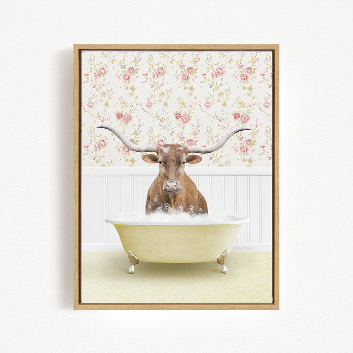 A brown cow with long horns is sitting in a white bathtub filled with bubbles, against a floral wallpaper background.