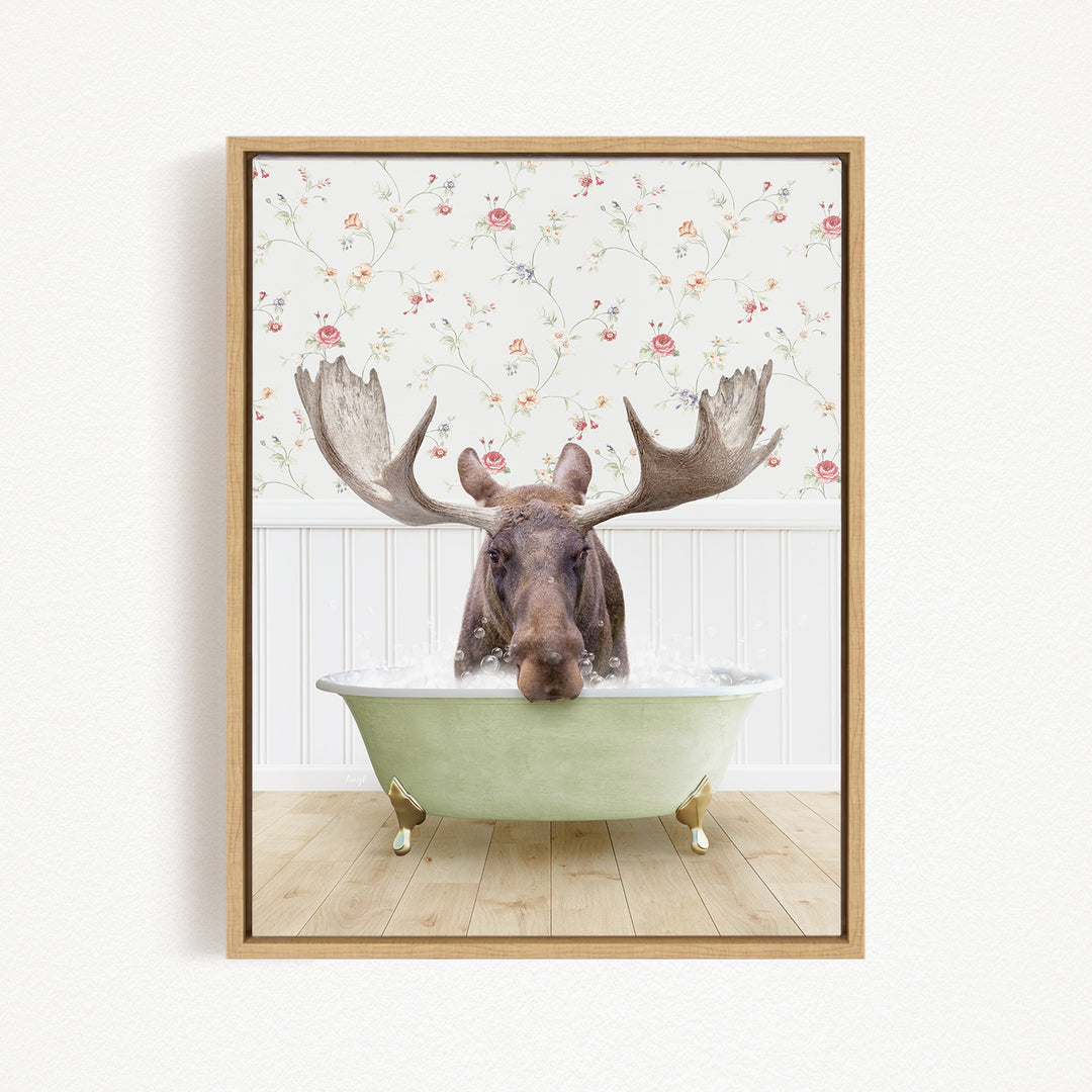 A moose with large antlers is sitting in a green bathtub, surrounded by a floral wallpaper.