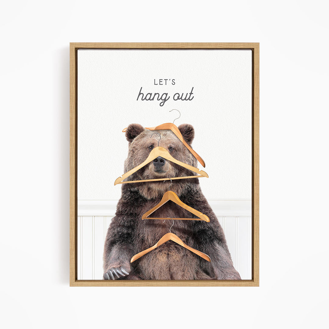 A framed image of a bear sitting on a white wall, with a pile of hanging clothes around its head.