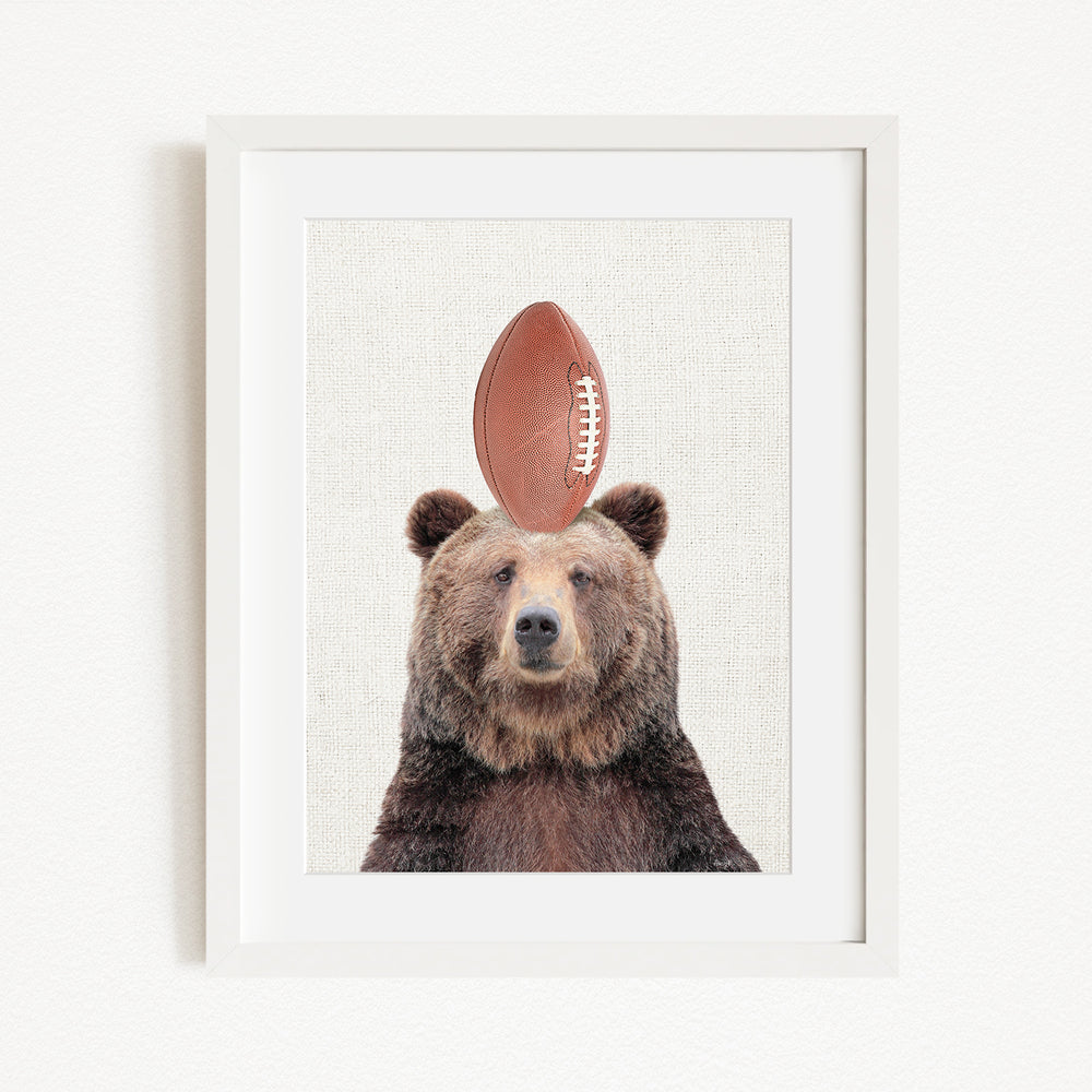 A framed image of a brown bear with a football on its head.