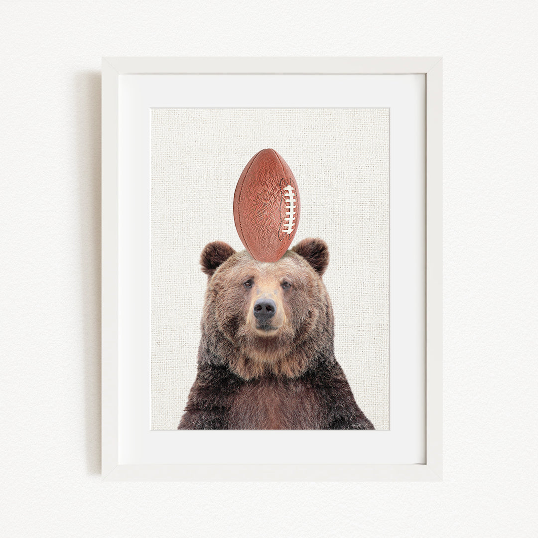 A framed image of a brown bear with a football on its head.