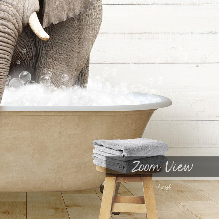 A large elephant is standing in a bathtub filled with bubbles, with a wooden stool and towels nearby.