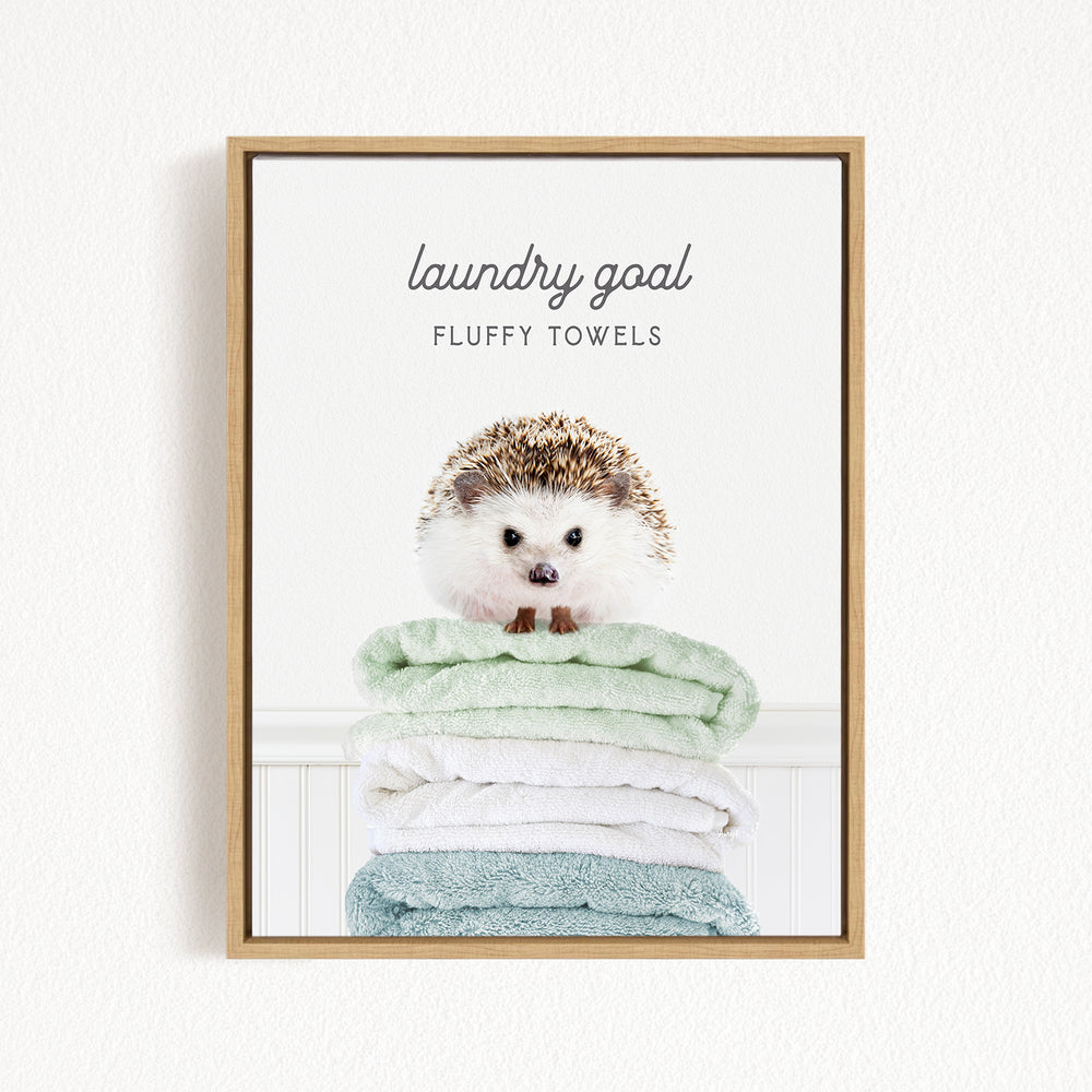 A framed image of a hedgehog sitting atop a stack of fluffy towels, with the text "laundry goal" and "fluffy towels" written above it.
