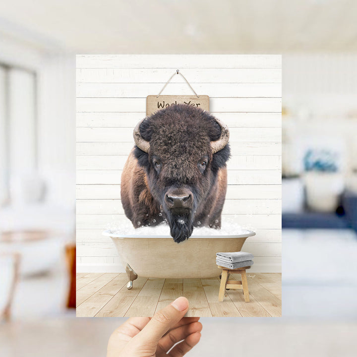 A hand holds up a framed image of a bison in a bathtub, with a sign above it that says "Wax on your face".