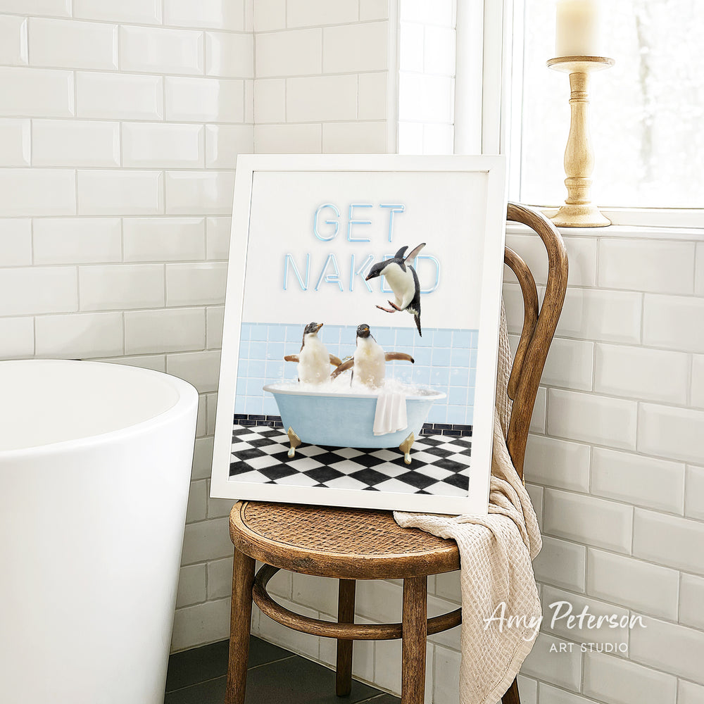 A framed print of a penguin bathtub with two penguins sitting in it, accompanied by the text "GET NAKED" in the top left corner.