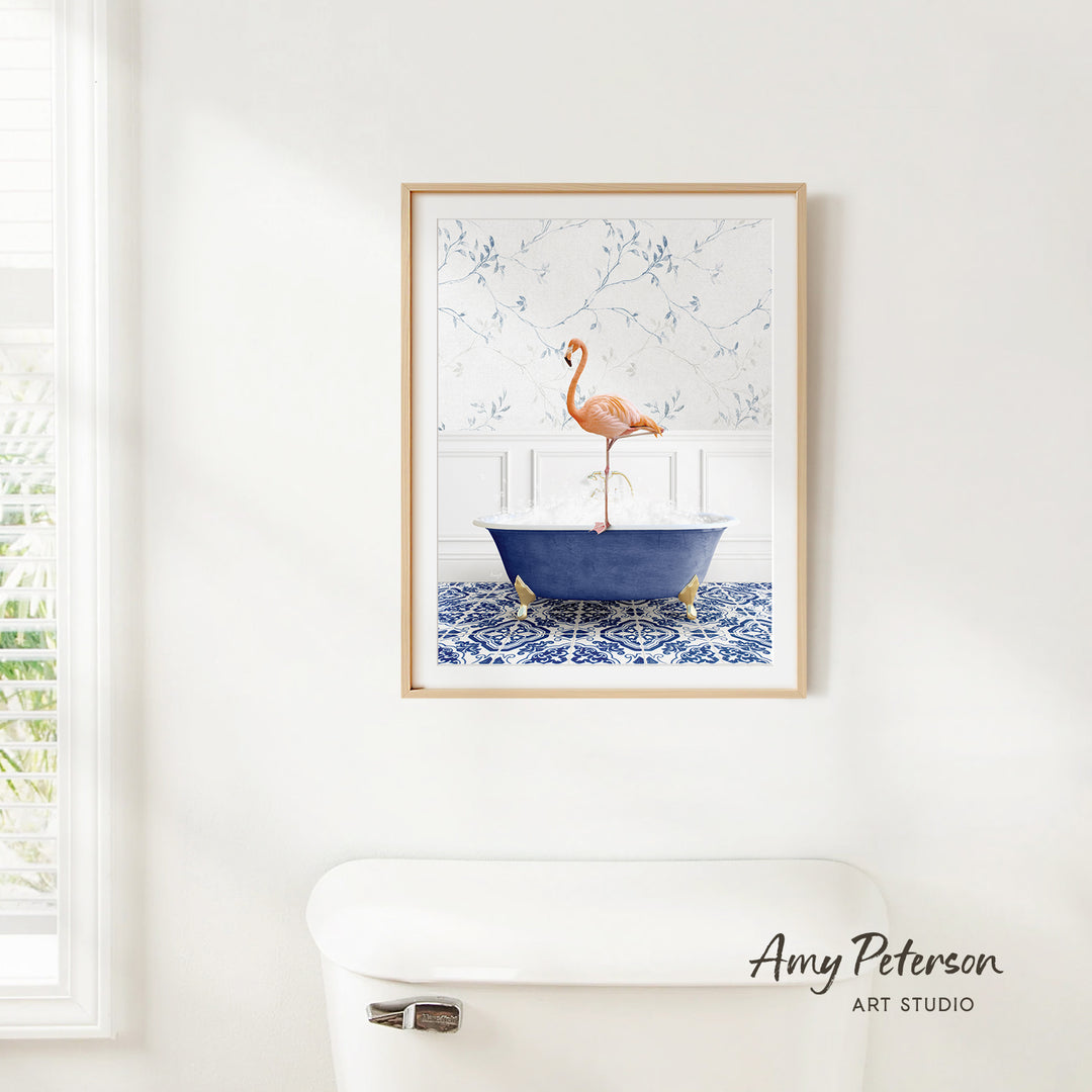 A framed painting of a pink flamingo standing on a blue bathtub is hanging on a white wall in a bathroom.