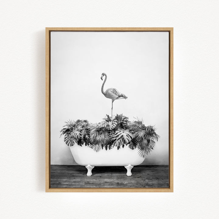 A black and white photograph of a flamingo standing on a white bathtub filled with tropical plants.