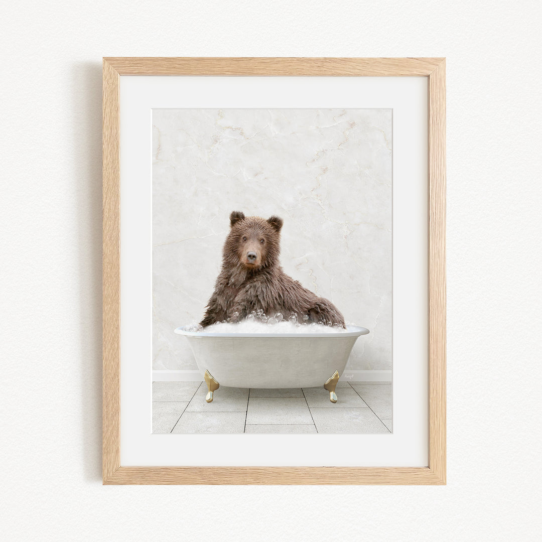 A brown bear sitting in a white bathtub filled with bubbles, looking directly at the camera.