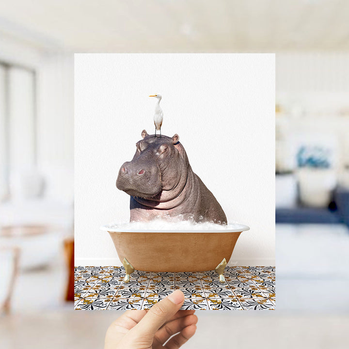 A hand holds up a framed image of a hippopotamus sitting in a bathtub, with a seagull perched on its head.