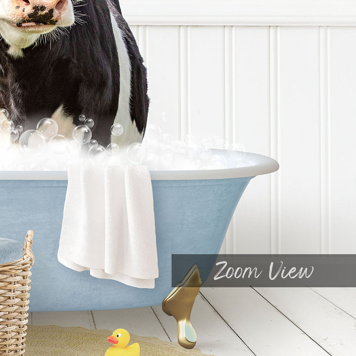 A black and white cow is sitting in a blue bathtub filled with bubbles, with a yellow rubber duck nearby.