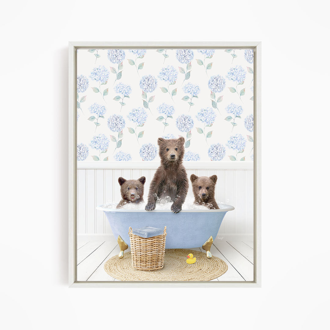 A framed image depicting three bears sitting in a blue bathtub, with a blue and white floral pattern on the wall behind them.
