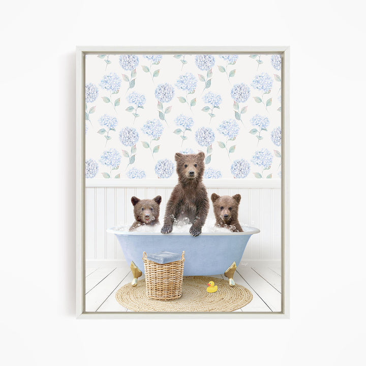 A framed image depicting three bears sitting in a blue bathtub, with a blue and white floral pattern on the wall behind them.