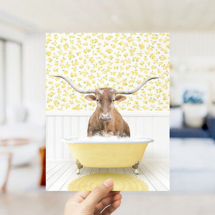 A brown cow with large horns is sitting in a yellow bathtub filled with water, surrounded by a yellow and white floral pattern on the wall behind it.