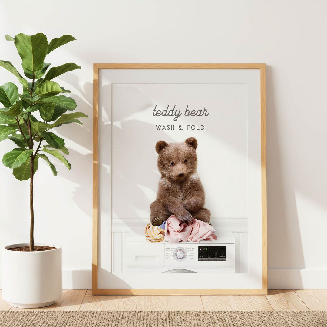 A framed image of a teddy bear sitting on a washing machine, with the text "teddy bear WASH & FOLD" displayed above the bear.