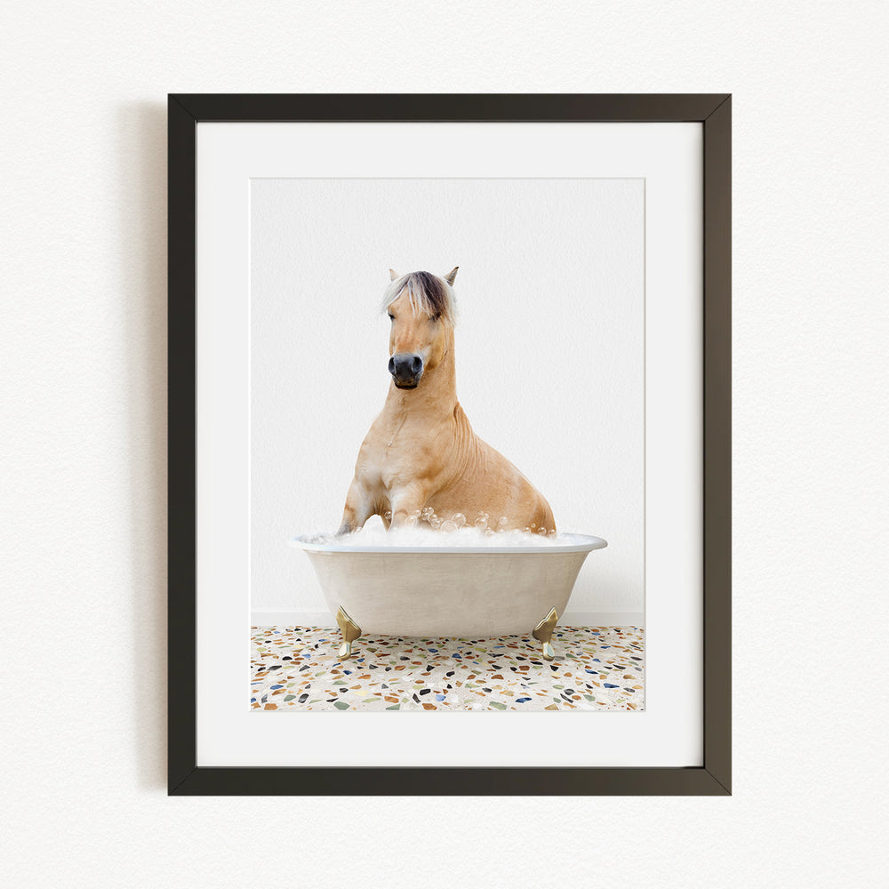 A light brown horse is sitting in a white bathtub filled with water, surrounded by a speckled floor.