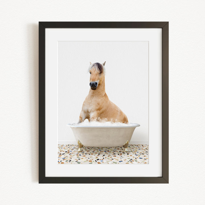 A light brown horse is sitting in a white bathtub filled with water, surrounded by a speckled floor.