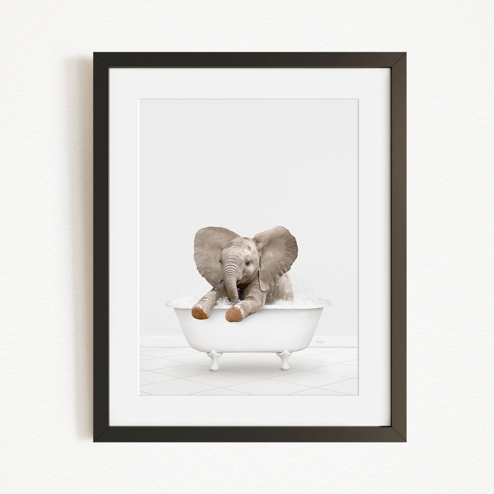 A baby elephant sitting in a white bathtub, with its trunk raised and ears spread out.