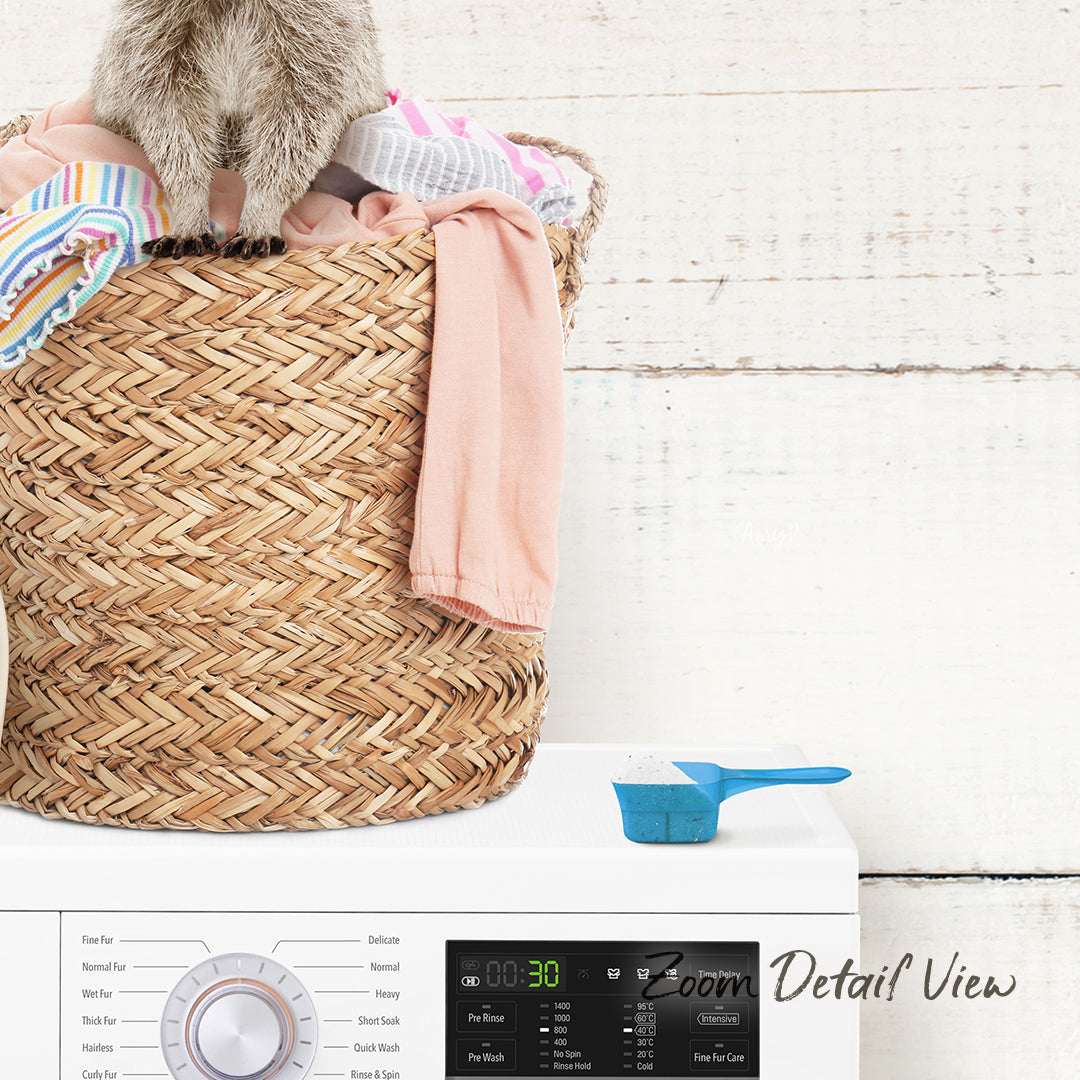 A laundry basket filled with clothes sits on top of a white washing machine, with a blue scoop resting on the front of the machine.