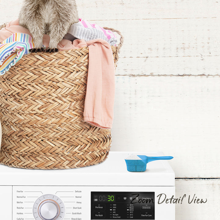 A laundry basket filled with clothes sits on top of a white washing machine, with a blue scoop resting on the front of the machine.
