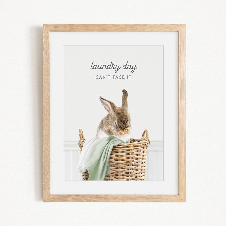 A framed image of a rabbit sitting in a wicker basket, with the text "laundry day can't face it" written above the rabbit.