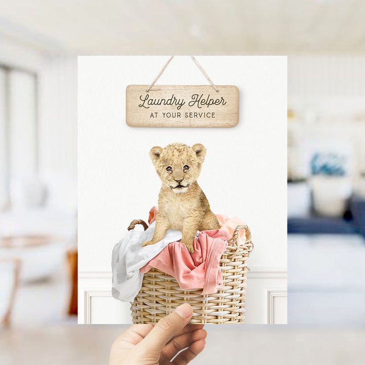 A hand holding a sign that says "Laundry Helper at your service" with a picture of a young lion cub sitting in a basket of clothes.
