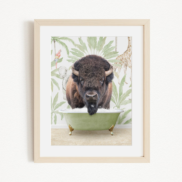 A framed image depicting a bison standing in a green bathtub, surrounded by tropical foliage and a giraffe.