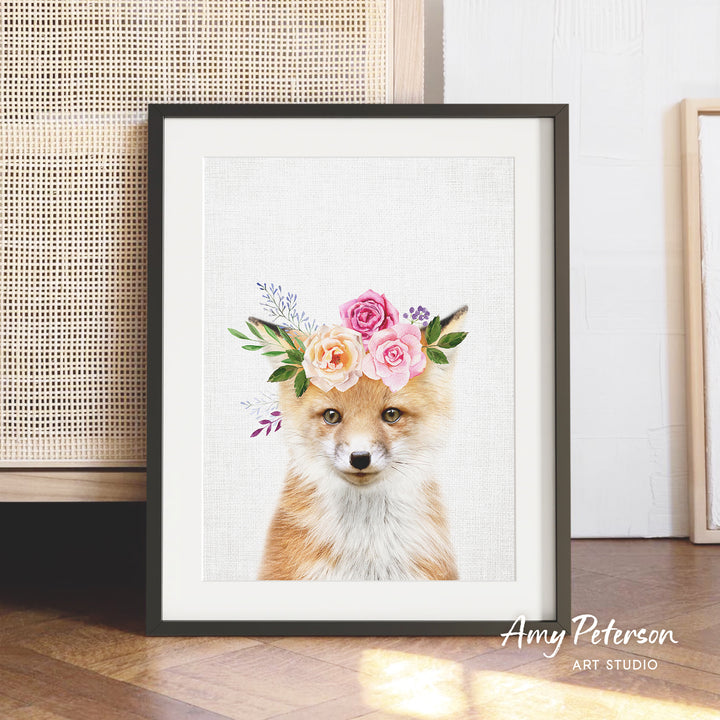 A framed print of a fox wearing a floral crown, with a white background and pink and orange flowers.