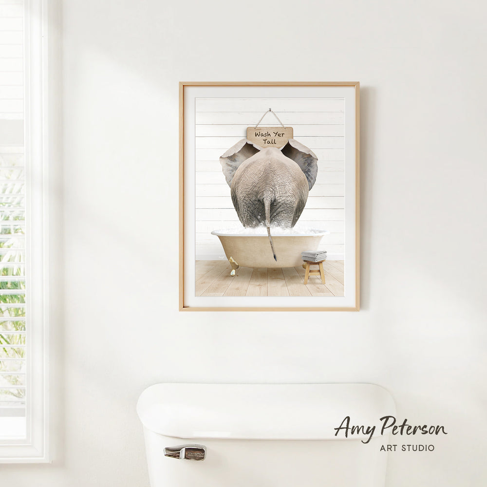 A framed image of an elephant sitting in a bathtub, with a sign hanging above it that says "Wash Your Tail".