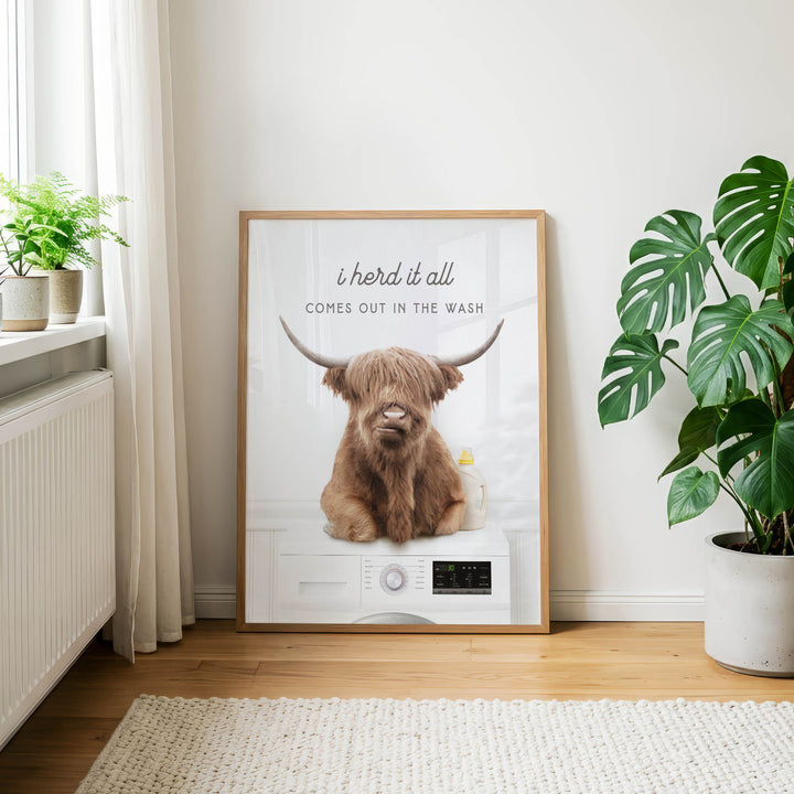 a framed poster with a cartoon image of a cow with horns, sitting on a washing machine, and the text "I herd it all comes out in the wash".