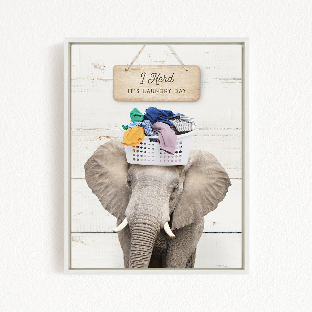 A gray elephant holding a basket of laundry on its head, with a wooden sign above that says "It's laundry day".