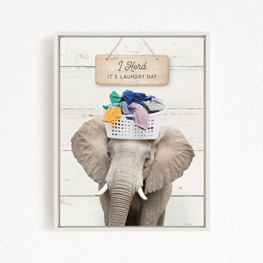 A gray elephant holding a basket of laundry on its head, with a wooden sign above that says "It's laundry day".