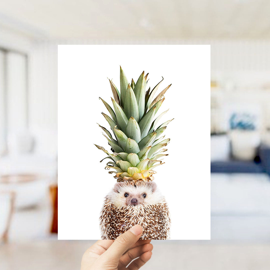 A hand holds up a photograph of a hedgehog wearing a pineapple crown.